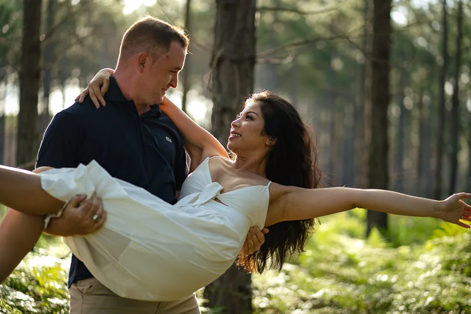 Jake carrying Romarie through the pines, arms flung wide
