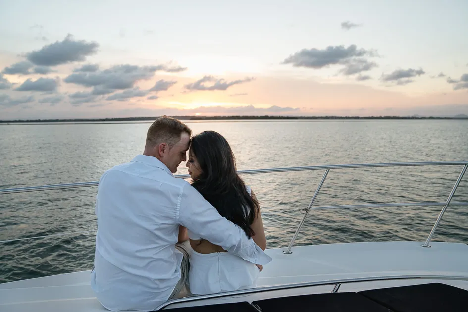 Romarie and Jake sitting together at the bow, facing the sunset across the water