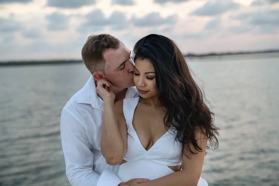 Jake kissing Romarie’s cheek, the water silver behind them