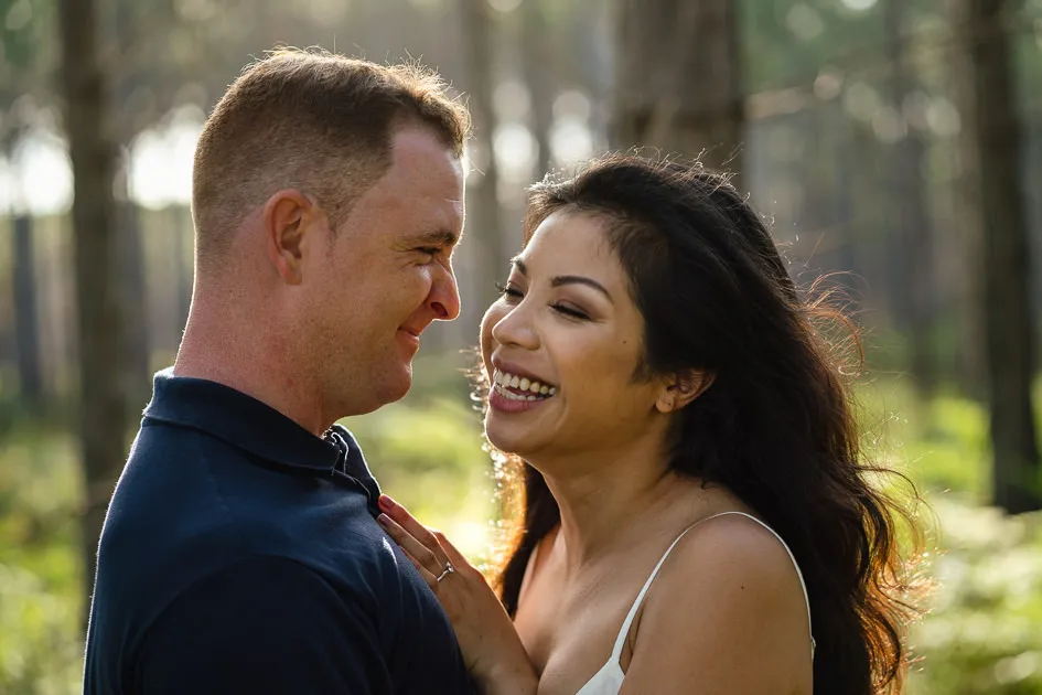 Romarie laughing as Jake leans in, the low sun through the trees
