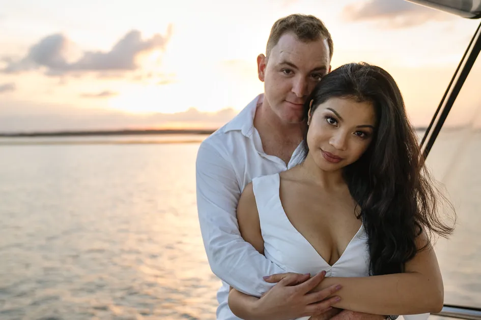 Romarie and Jake on the deck of a boat at sunset, the water calm behind them