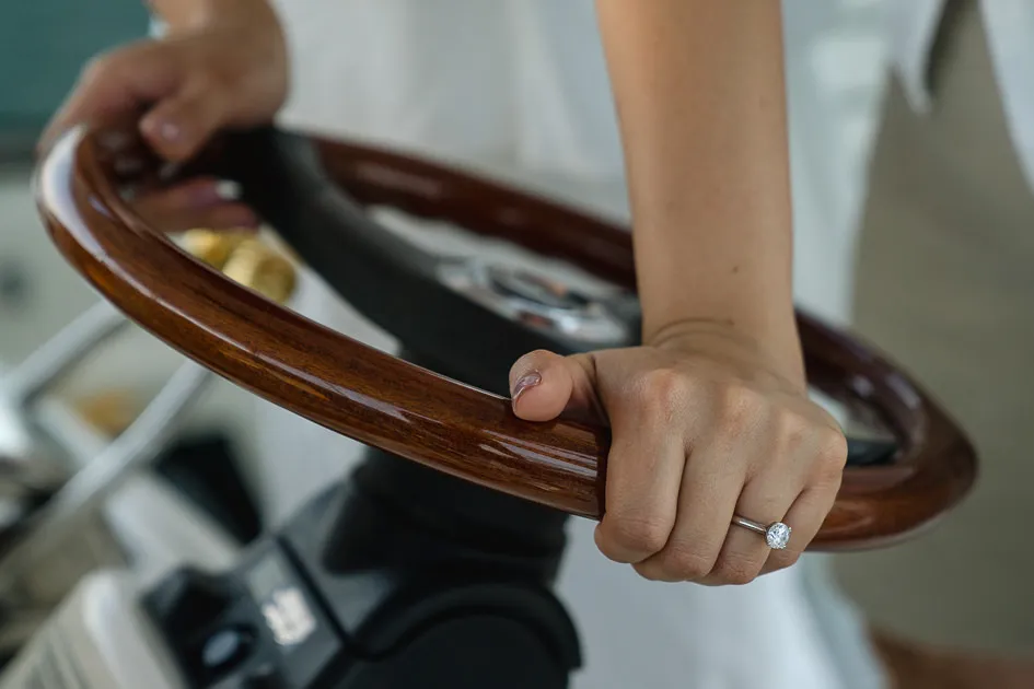 An engagement ring on a hand at the wooden wheel of a boat
