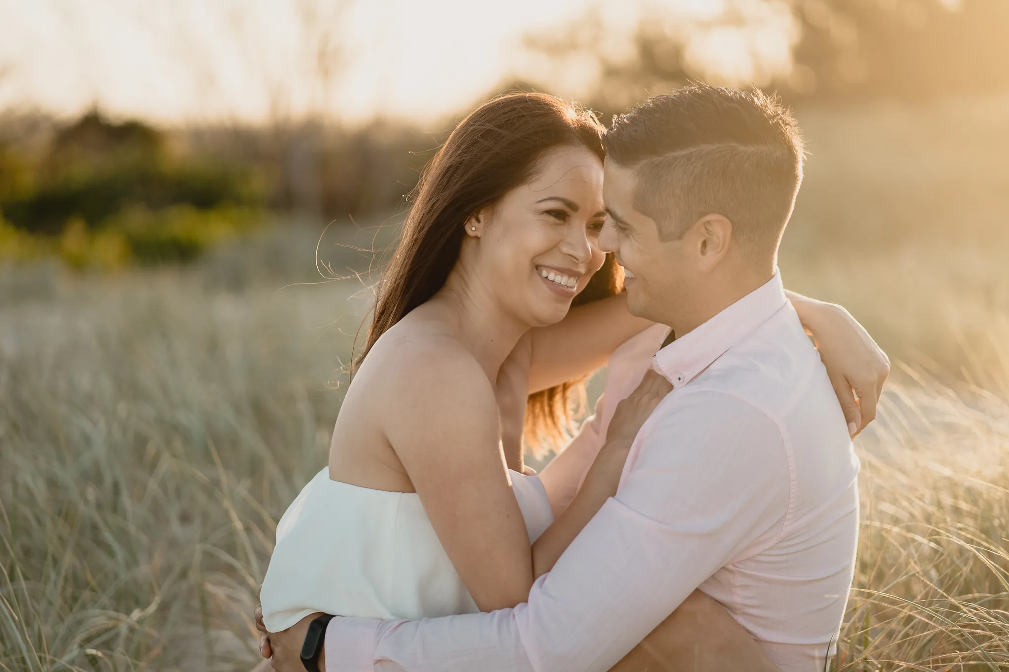 Rafaela and Mark laughing cheek to cheek in the dune grass at golden hour