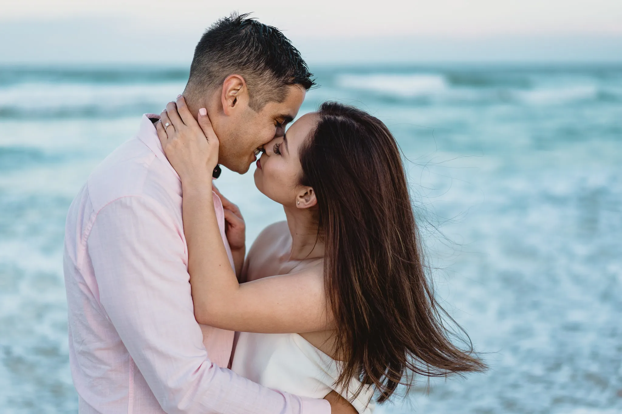 Rafaela and Mark kissing on the shore, the wind lifting Rafaela’s hair