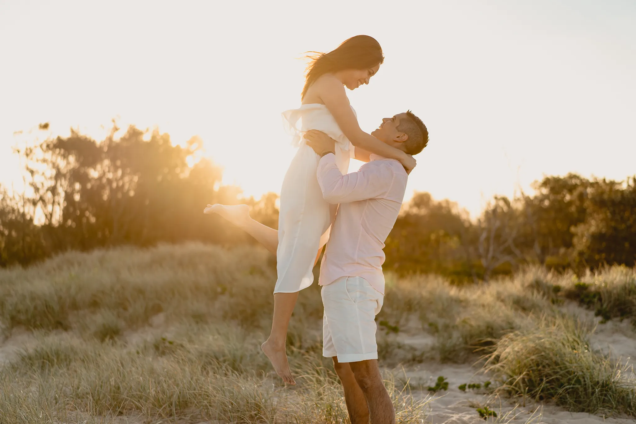 Mark lifting Rafaela into the air on the dunes, the sun setting behind them