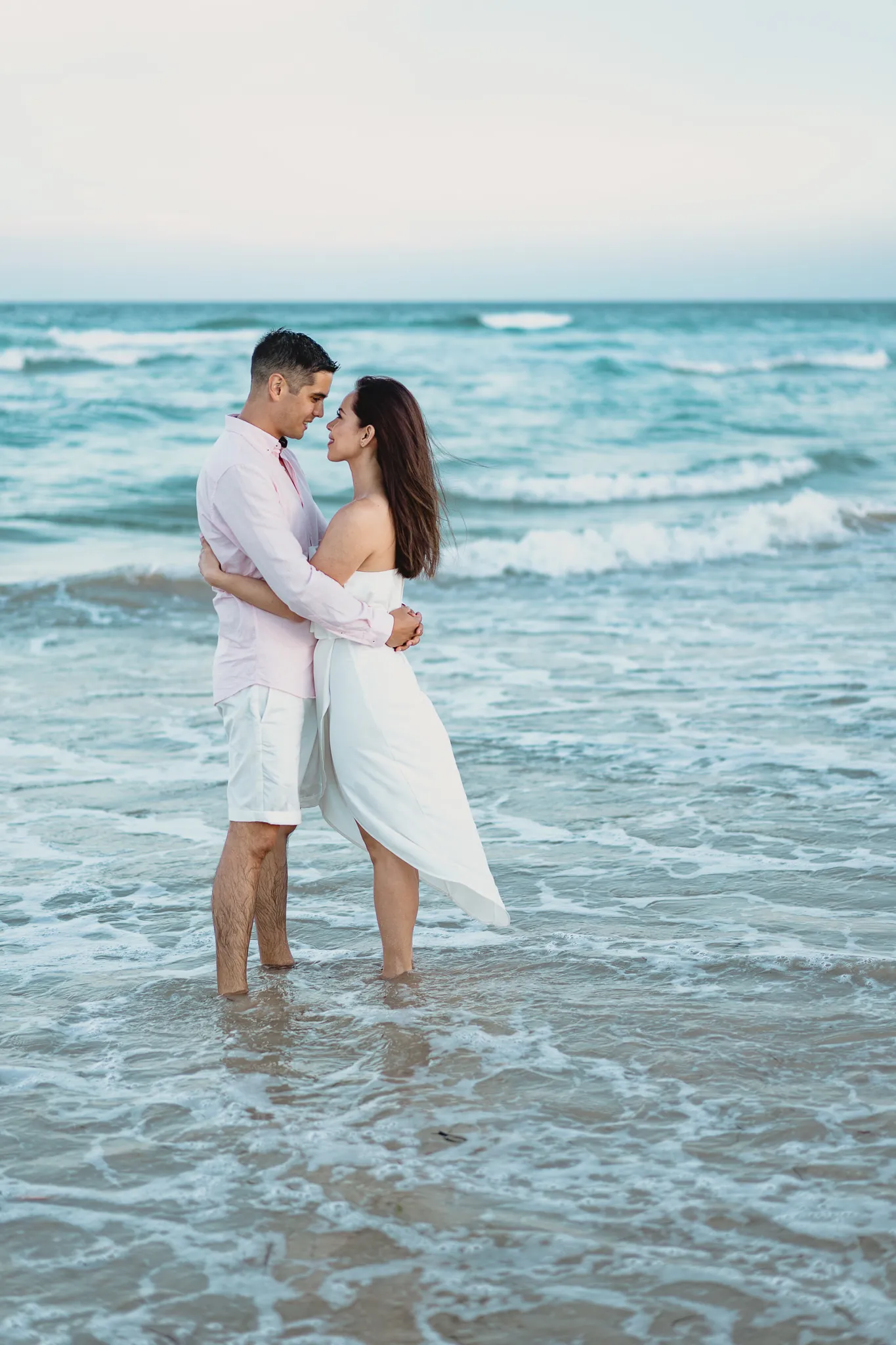 Rafaela and Mark holding each other in the shallows at blue hour, waves rolling in behind them
