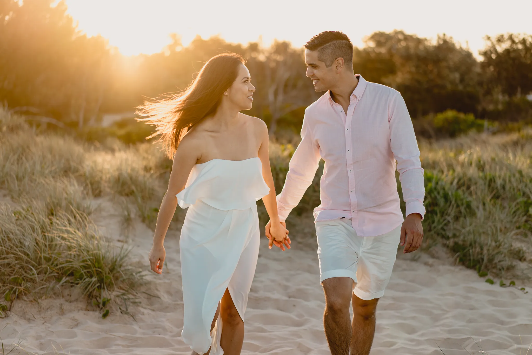 Rafaela and Mark walking hand in hand down through the dunes, backlit by the setting sun