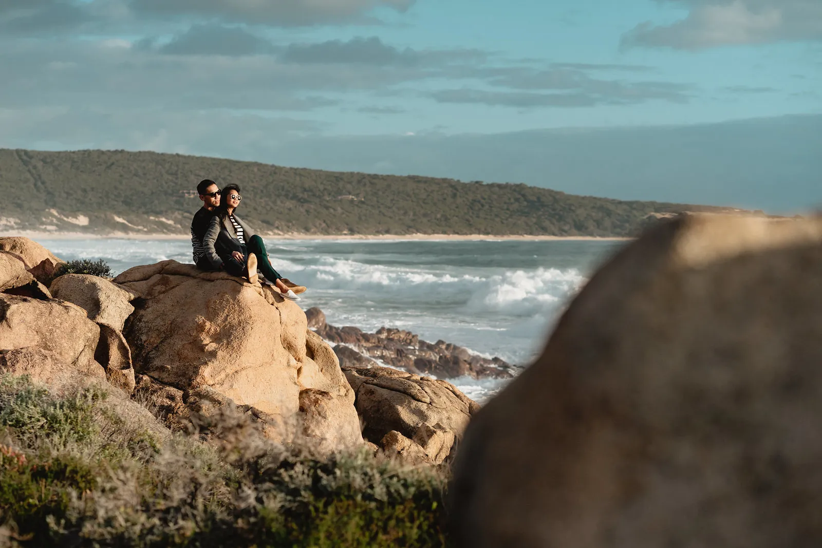 Zaneta and Vryan sitting on a boulder above the surf