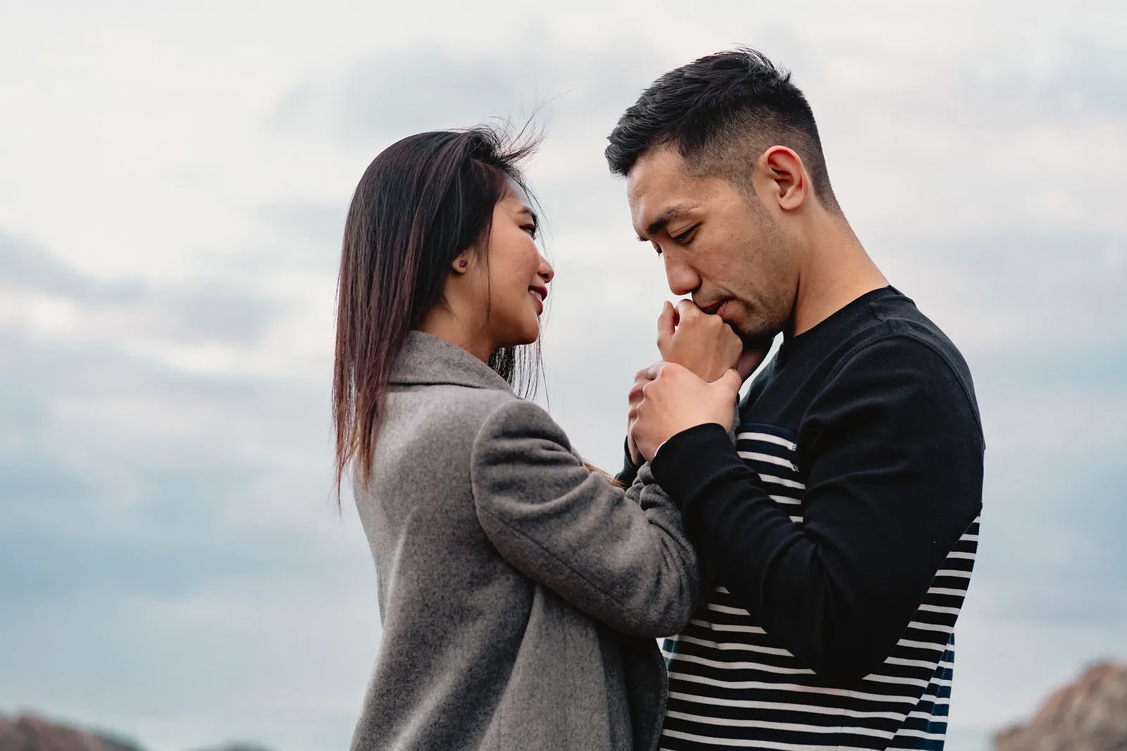 Vryan kissing Zaneta’s hands on the windswept coast, photographed by Sean