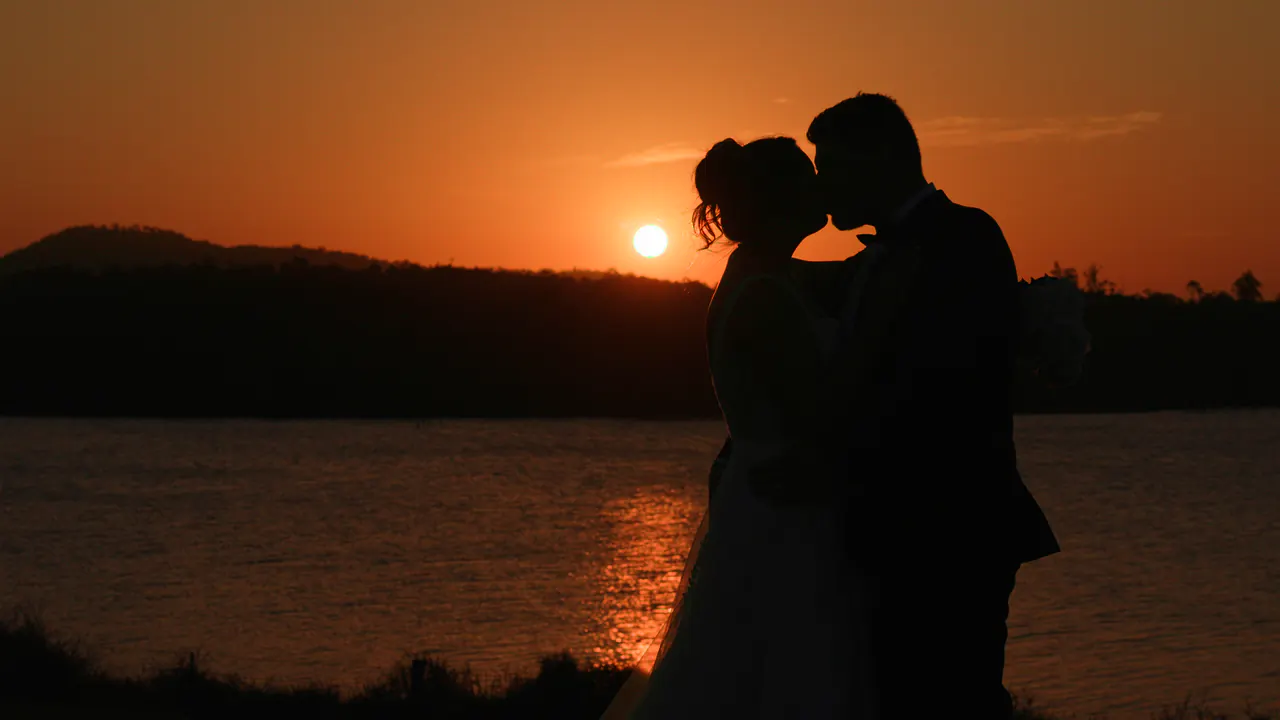 Lauren and Mike kissing in silhouette by the water, the sun setting beside them