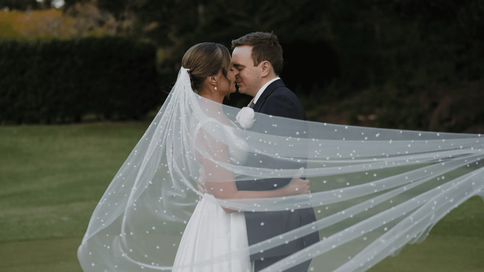 Lucy and Oliver kissing as her veil lifts on the wind