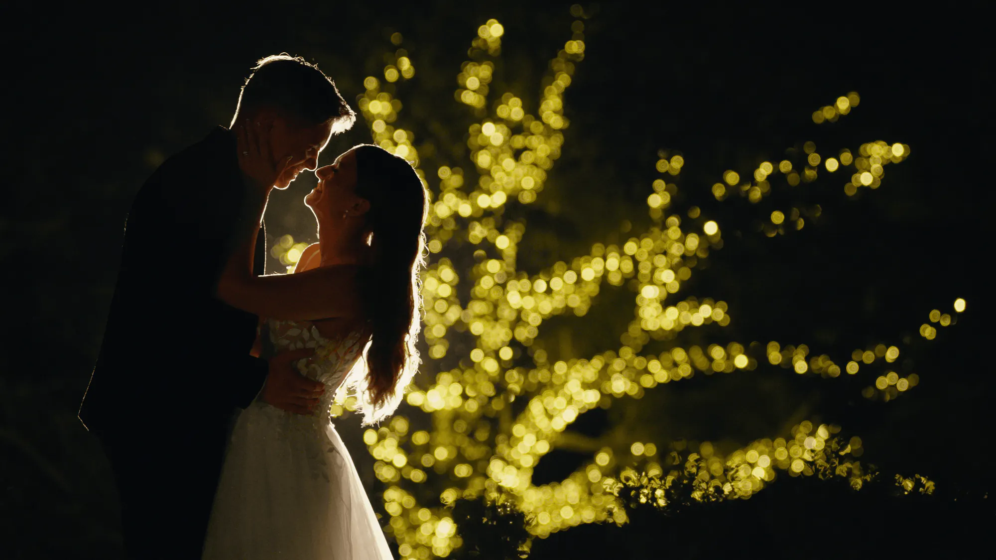Nicaela and James embracing at night beneath fairy lights